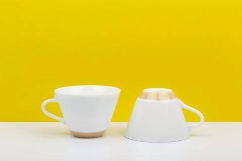 Two white ceramic coffee cups on white table against bright yellow background Stock Photos