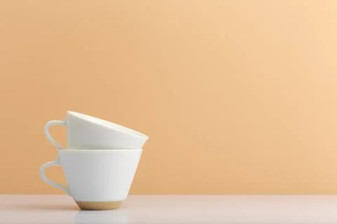 Two white ceramic cups one in another on white table against light beige Stock Photos