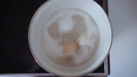 Two white chicken eggs are boiled in boiling water from which comes thick steam. Stock Footage 112043632