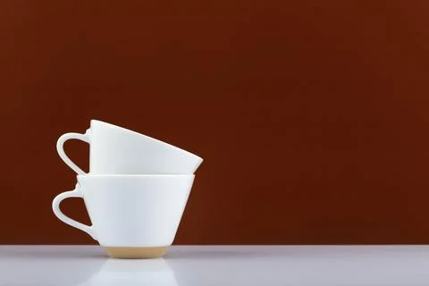 Two white coffee cups on in another on white table against brown background with Stock Photos