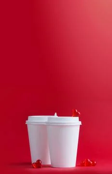 Two white coffee cups next to glass hearts on a red background. Mockup. Stock Photos