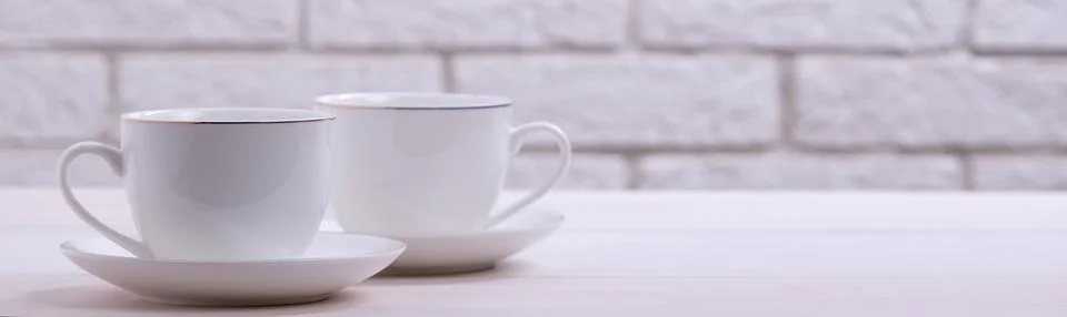 Two white coffee cups on a table against a brick wall Stock Photos
