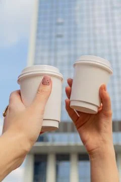 Two white cups with coffee to go in female hands against the background of city Stock Photos