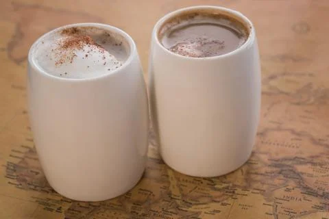 Two white cups of coffee stand on a world map against a light background Stock Photos