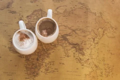 Two white cups of coffee stand on a world map against a light background Photos