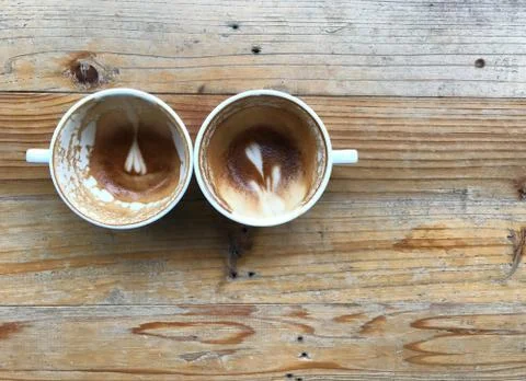 Two white cups of finished latte coffee on light brown wooden table Stock Photos