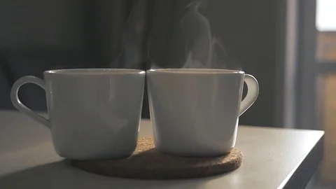 Two white cups of hot tea stand on the table, with a beautiful curly steam. Slow Stock Footage 74992195