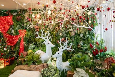 Two white deer statues sit among green plants and holiday decorations, with.. Stock Photos