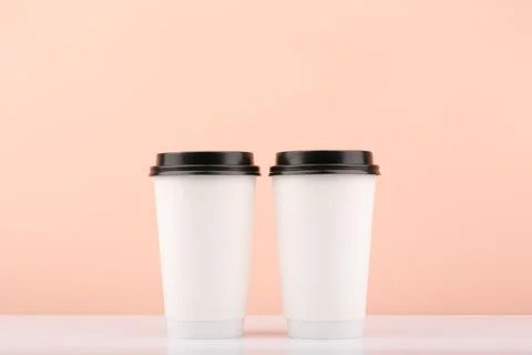 Two white disposable coffee or tea cups against beige background with copy space Stock Photos