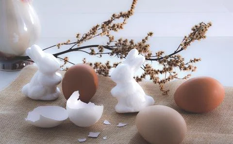 Two white Easter bunnies next to brown eggs on a beige tablecloth stand on .. Stock Photos