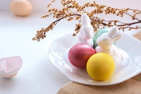 Two white Easter bunnies next to Easter eggs stand on a white plate on the .. Stock Photos