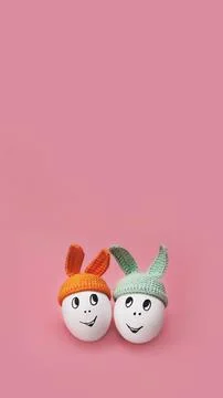 Two white eggs in beanie with rabbit ears and cheerful faces on pink background Stock Photos
