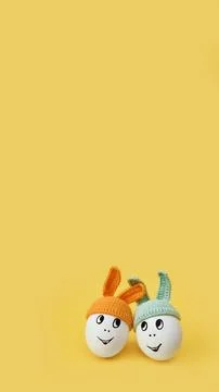 Two white eggs in beanie with rabbit ears and cheerful faces on yellow Stock Photos