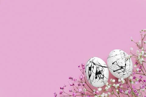 Two white eggs in black spots and flowers on a pink background with a copy of Stock Photos