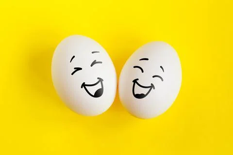 Two white eggs on yellow background concept. Emotions laughter and happiness. Stock Photos