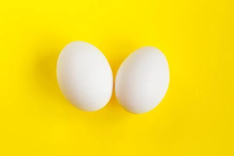 Two white eggs on a yellow background. Creative concept in the style of minim Stock Photos