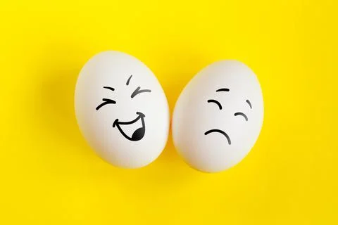 Two white eggs on yellow background concept. Emotions laughter and sadness. F Stock Photos
