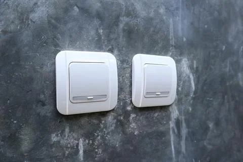 Two white electrical light switches mounted on a raw polished concrete wall.. Stock Photos