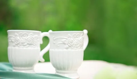 Two white empty cups on table against green background. Stock Photos