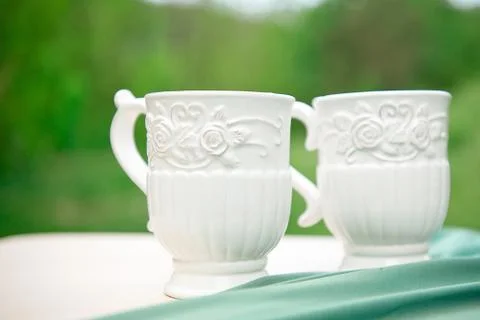 Two white empty cups on table against green background. Stock Photos