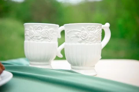 Two white empty cups on table against green background. Stock Photos