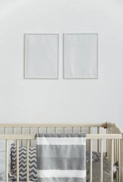 Two white empty wall frames above infant baby cot bed with gray blanket Stock Photos
