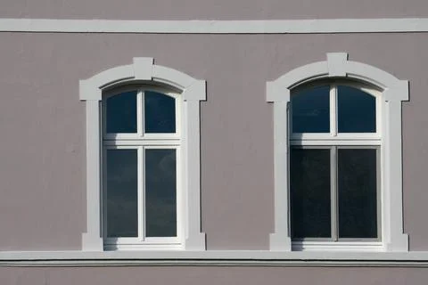 Two white-framed windows sit on a gray wall of a building. Fotos Stock