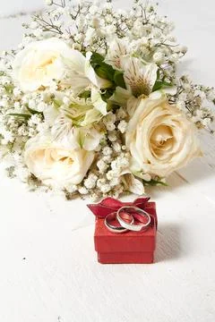 Two white gold rings of different sizes lie on a red box, the bride's bouqu.. Stock Photos