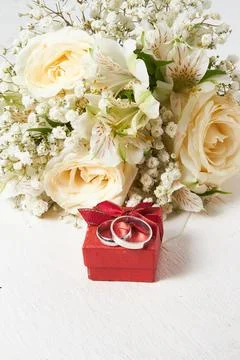 Two white gold rings of different sizes lie on a red box, the bride's bouqu.. Stock Photos