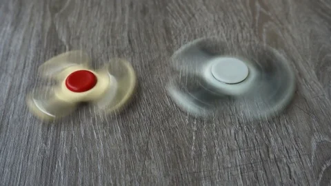 Two white hand spinner spinning on grey background or fidget spinners Stock Footage 76543443
