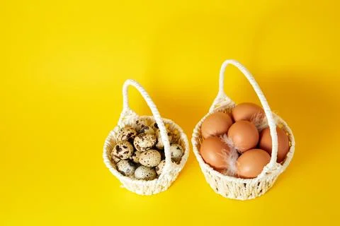 Two white handmade straw basket full of hen and quail eggs on yellow backgrou Stock Photos