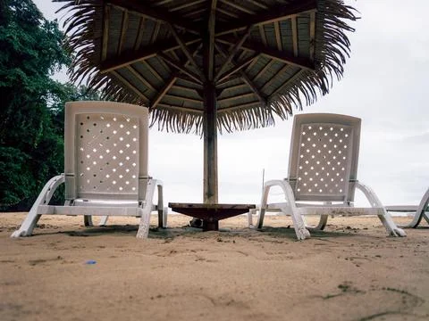 Two white lounge chairs sit on sandy beach Photos