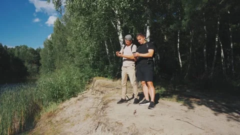 Two white men at lake lookout checking route and view, shoreline reeds and birch Stock Footage 323492549