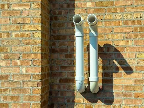 Two white pipes extend from a brick wall, casting clear shadows. The sunlight 스톡 사진