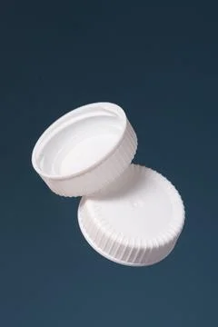 Two white plastic bottle caps on a blue background. Front and back of the cap Foto stock