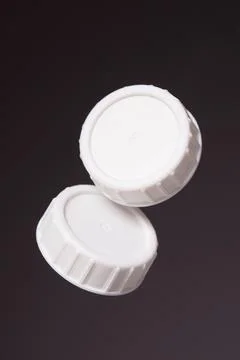 Two white plastic bottle caps on a black background. Stock Photos