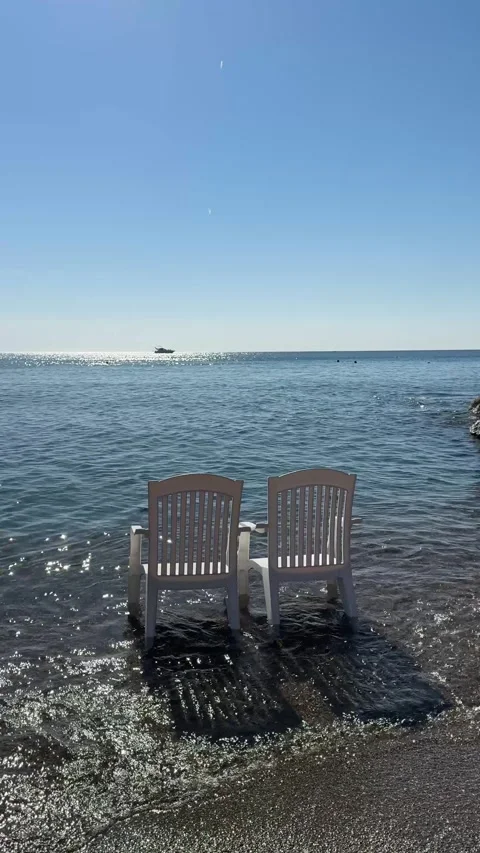 Two white plastic chairs stand in the water on a sandy beach, gently touched  Stock-Footage 305389449