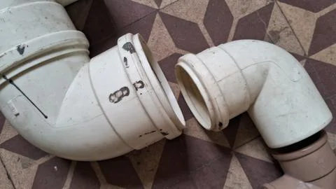 Two white plastic drainage pipes disconnected on a tiled floor Stock Photos