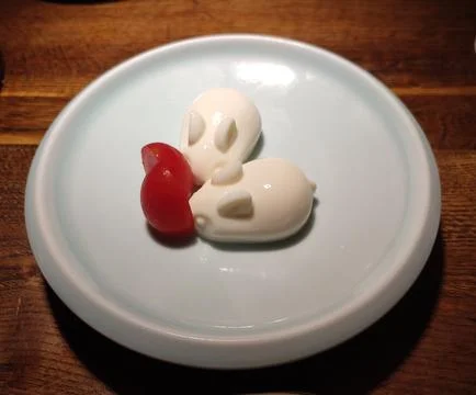 Two white pudding shaped like rabbits with tomato on the plate Stock Photos