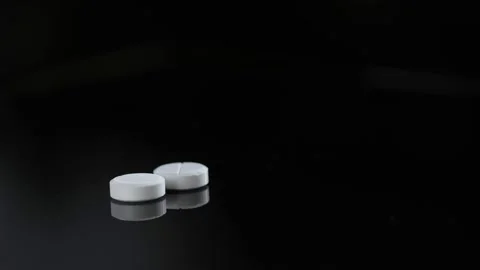 Two white round pills on a black background. white medical pills rotating Stock Footage 175221148