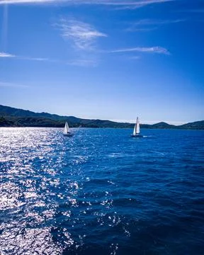 Two white sailing yachts on the background of a mountainous coastline. In the Stock Photos
