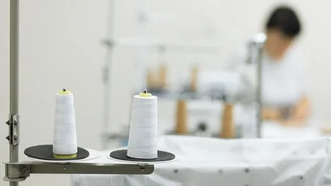 Two white sewing threads with large spool on blurred workshop background Stock Photos