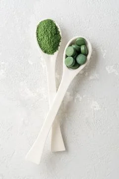 Two white spoons with chlorella or spirulina on a grey concrete background. Stock Photos