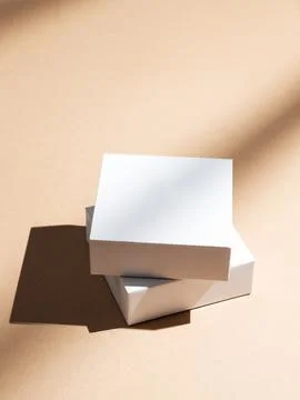 Two white square boxes on a beige background with natural light and shadows. Stock Photos