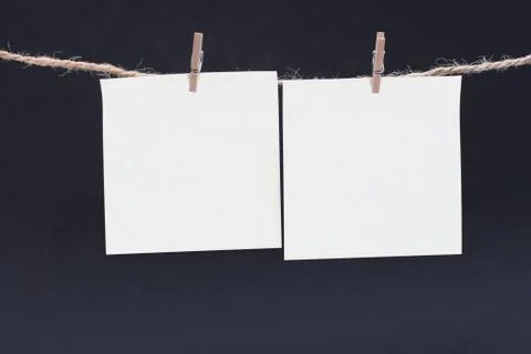 Two white square piece of note paper hangs on clothespins on a black background Stock Photos