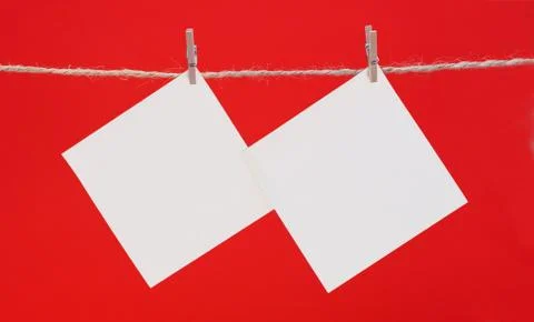 Two white square piece of note paper hangs on clothespins on a red background Stock Photos
