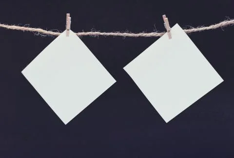 Two white square piece of note paper hangs on clothespins on a black backgrou Stock Photos