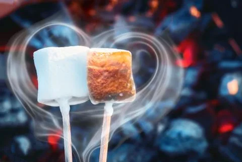 Two white sweet marshmallows roasting over fire flames. Smoke in form of heart Stock Photos