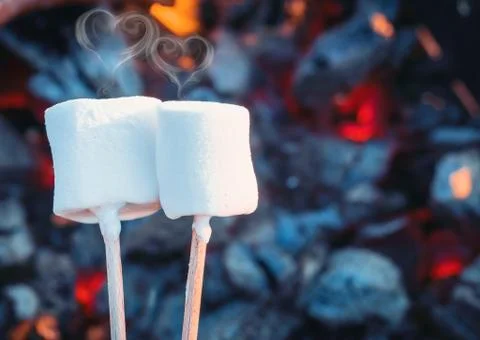 Two white sweet marshmallows roasting over fire flames. Smoke in form of hearts Stock Photos