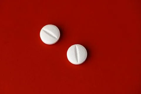 Two white tablets resting on a vibrant red surface create a striking visual.. Stock Photos